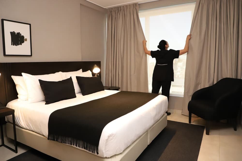 Quarto com cama grande, criado-mudo com abajur, cadeira e cortinas