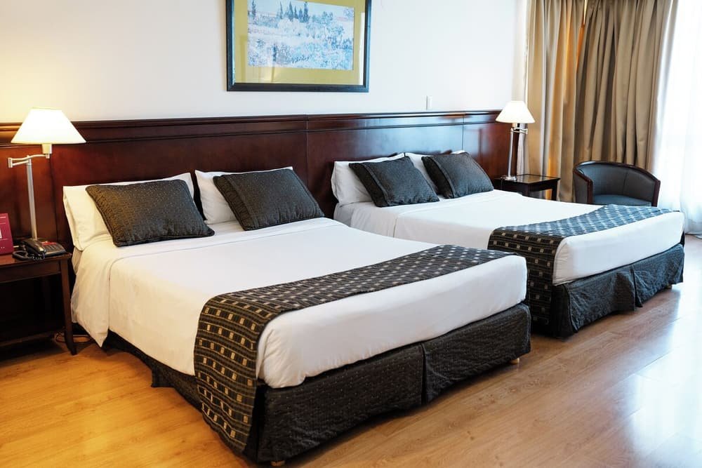 Quarto com duas camas, cabeceiras de madeira, abajures e um quadro