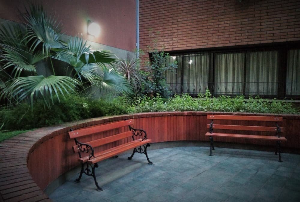 Patio con dos bancos de madera, pared de ladrillo y ventana