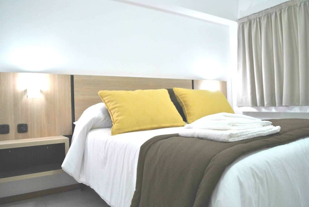 Habitación con cama, mesa de luz y ventana con cortinas