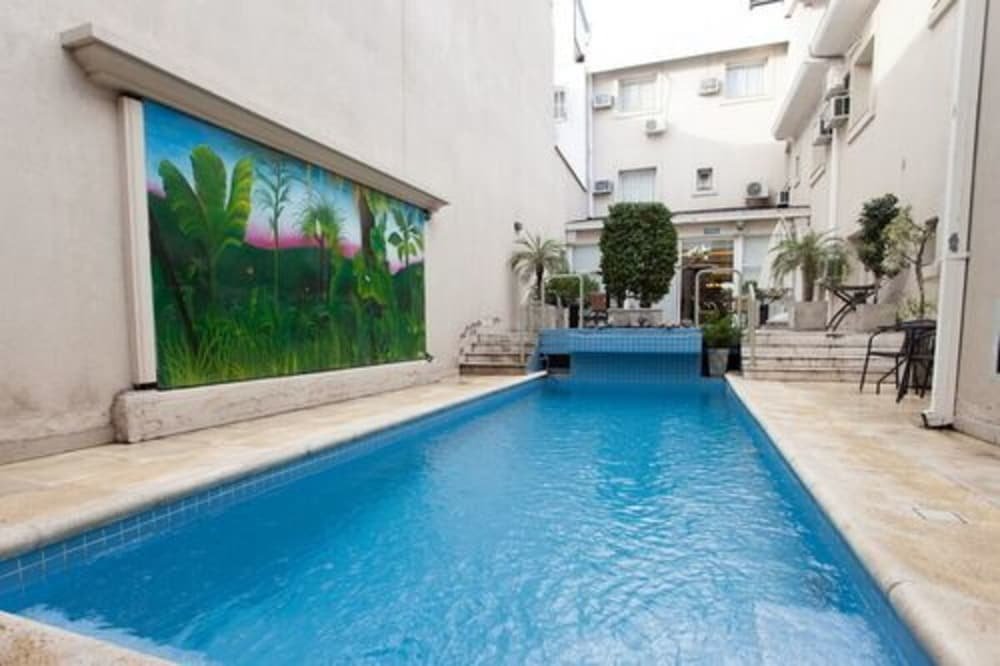 Pileta con un mural de plantas tropicales rodeada por el edificio y un jardín