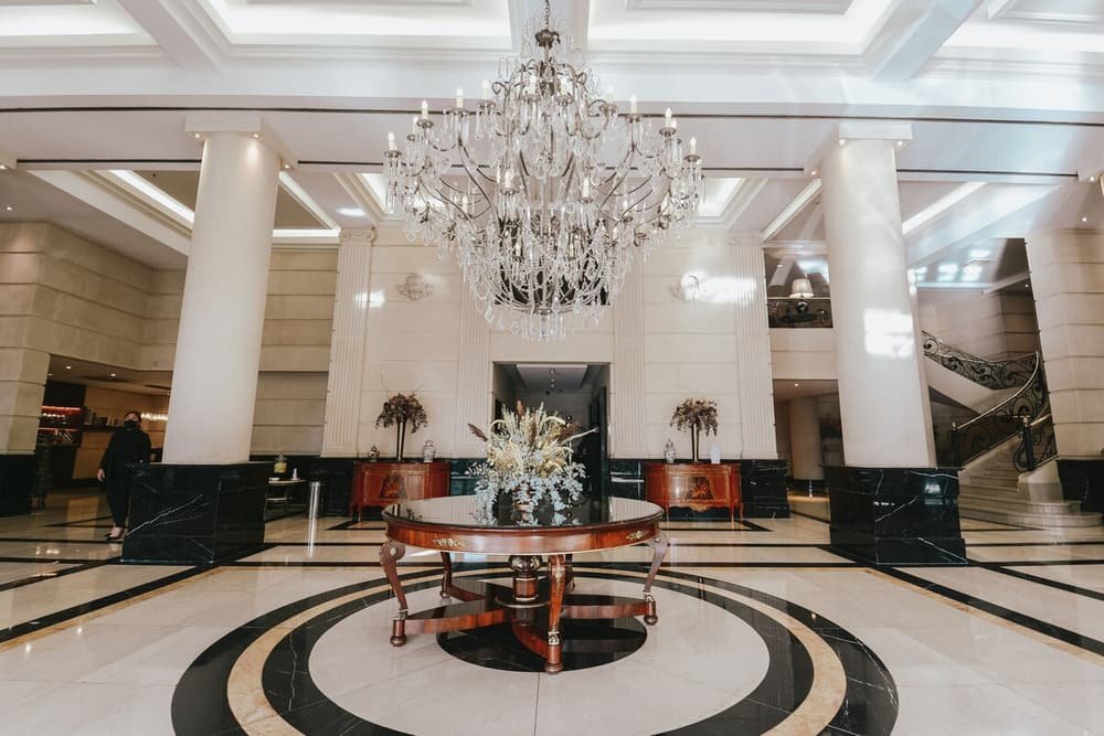 Grand lobby with a large chandelier, round table with vase and staircase