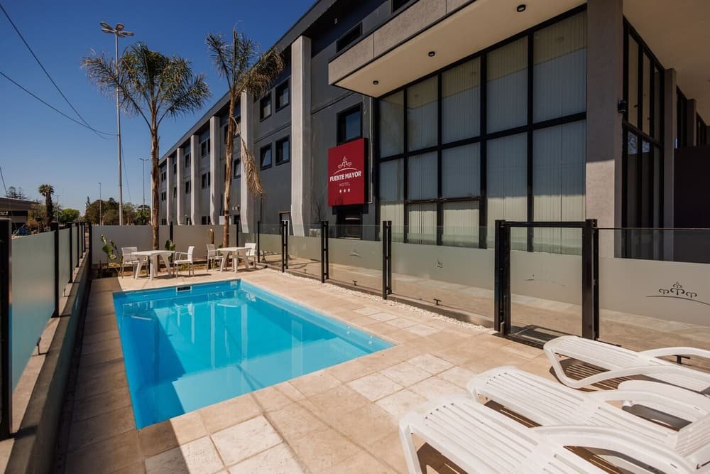 Piscina ao ar livre com cadeiras e mesas ao lado do prédio do hotel