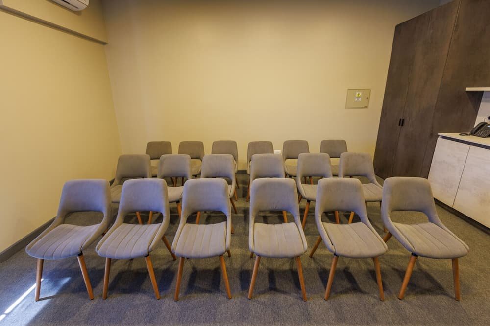 Sala de conferências com fileiras de cadeiras cinza e armário de madeira