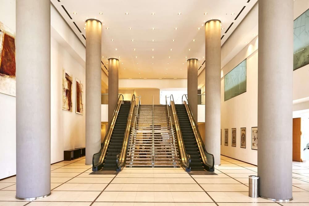 Lobby amplio con dos escaleras mecánicas, columnas grandes y piso de cerámica