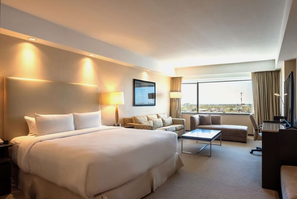Habitación con cama grande, sillón, escritorio y vista a la ciudad