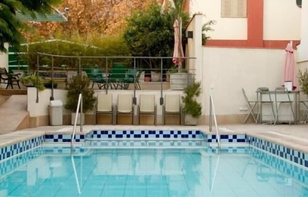 Swimming pool with a checkered tile border, chairs, tables and a small garden