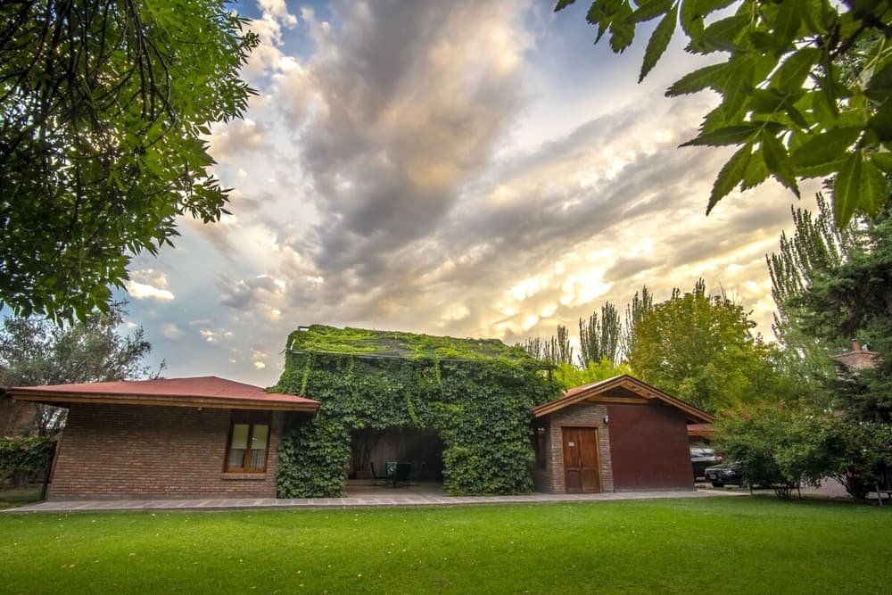 Casa de ladrillo con techo rojo rodeada de césped y árboles
