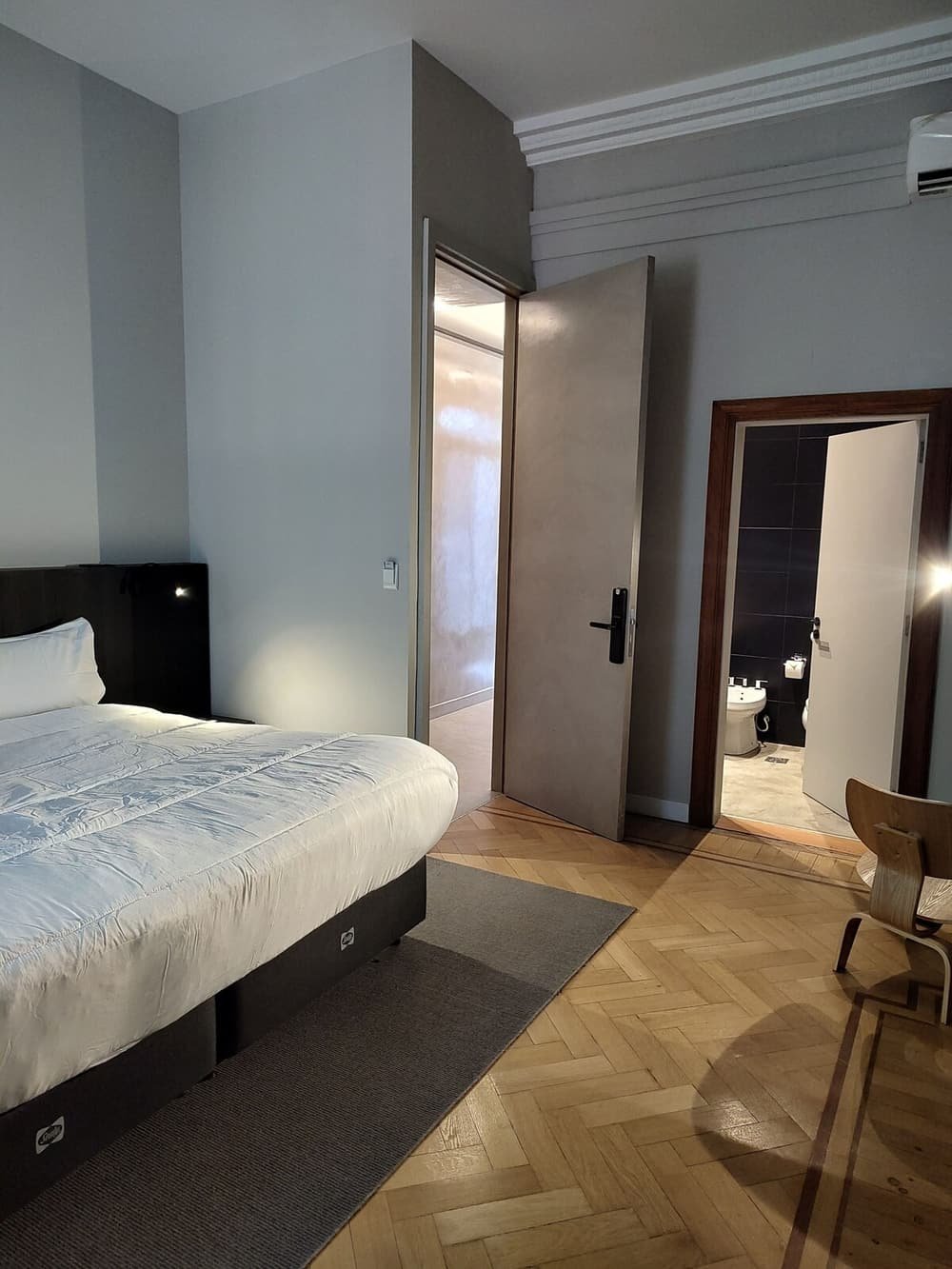 Dormitorio con cama, silla y placard, con el baño visible por la puerta