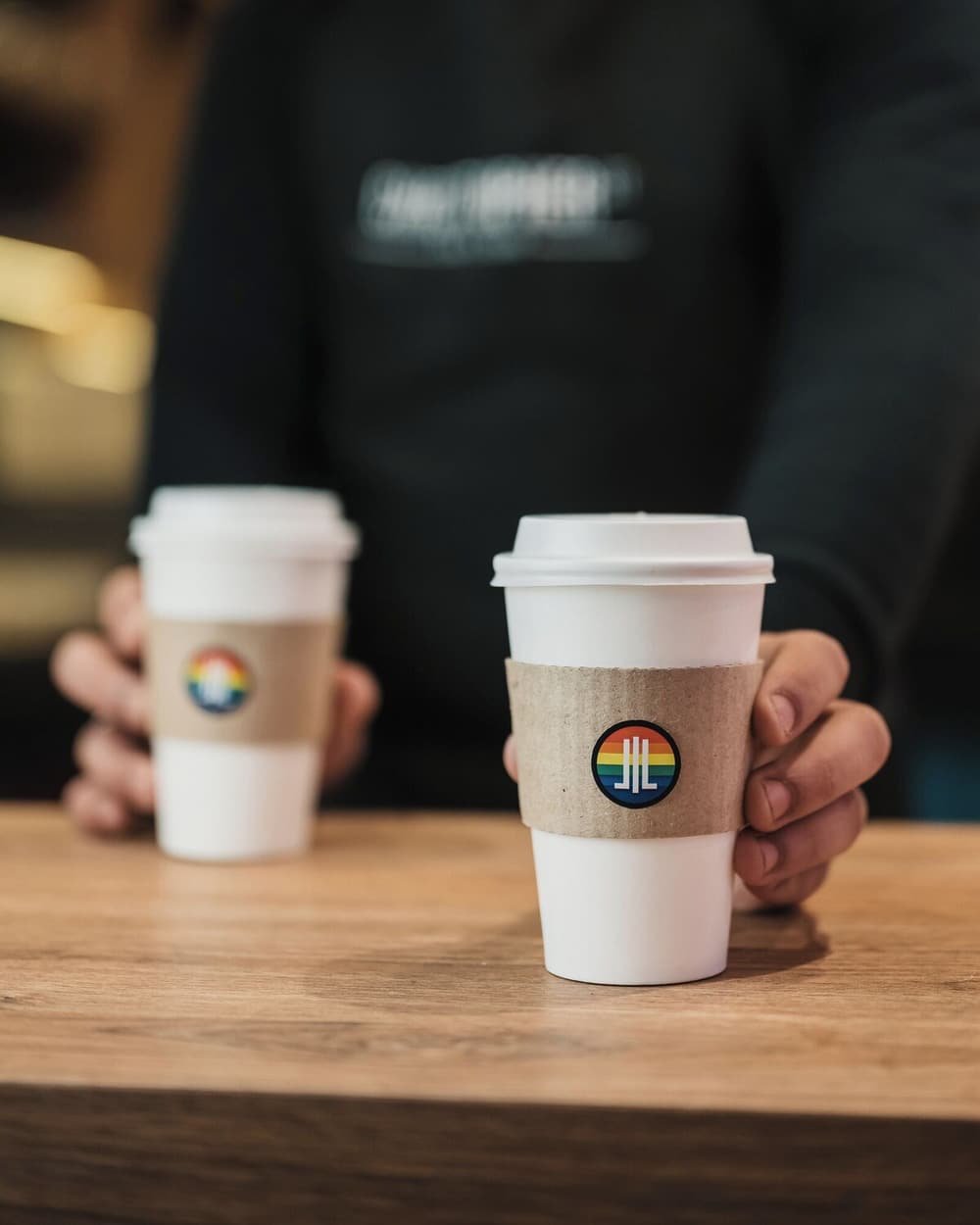 Dos vasos de café descartables con logo de arcoíris sobre una mesa de madera