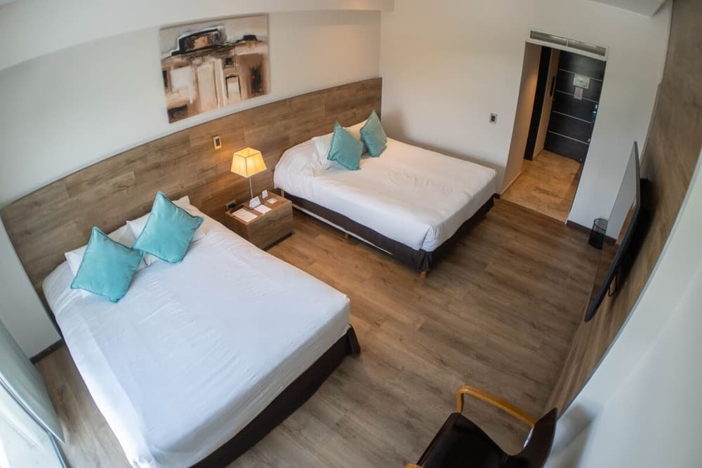 Quarto com duas camas, piso de madeira, abajur no criado-mudo e quadro