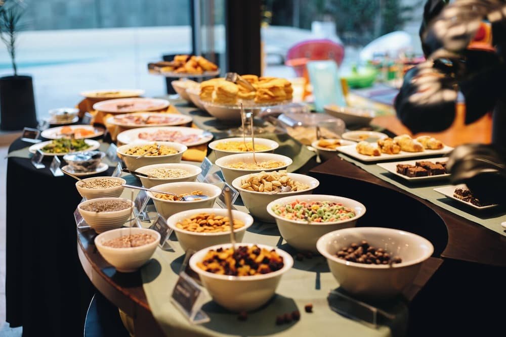 Buffet de café da manhã com variedade de alimentos e uma pessoa ao fundo
