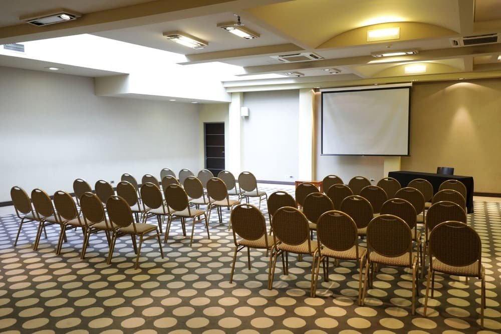 Sala de conferências com piso estampado, fileiras de cadeiras e tela de projeção