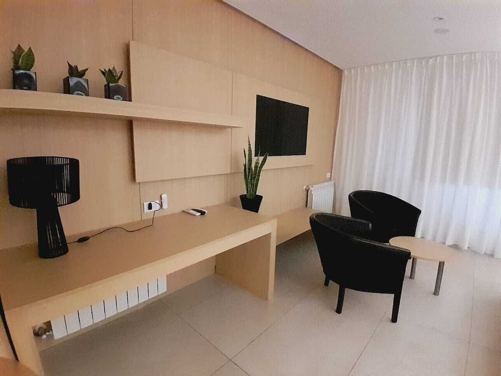 Living moderno con escritorio largo de madera, sillón negro y televisor en la pared