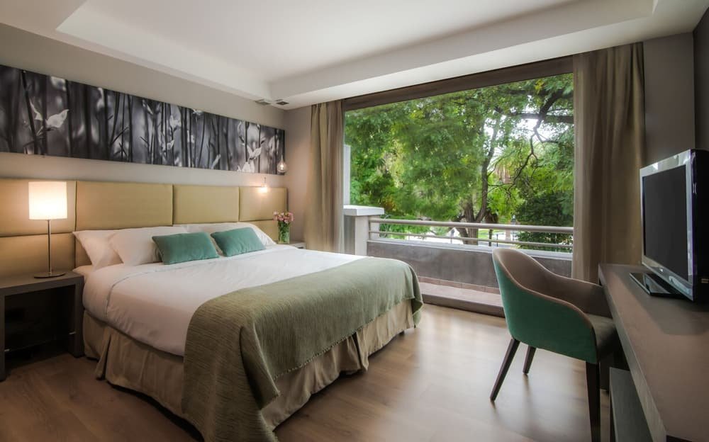 Habitación moderna con cama grande, escritorio con televisor y balcón con vista a árboles
