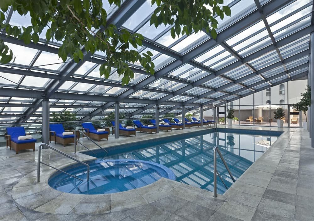 Piscina cubierta con reposeras azules y techo de vidrio