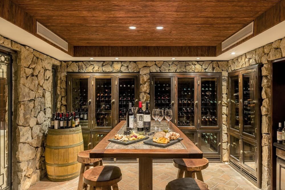 Salão de paredes de pedra com mesa de madeira posta, vinho e taças
