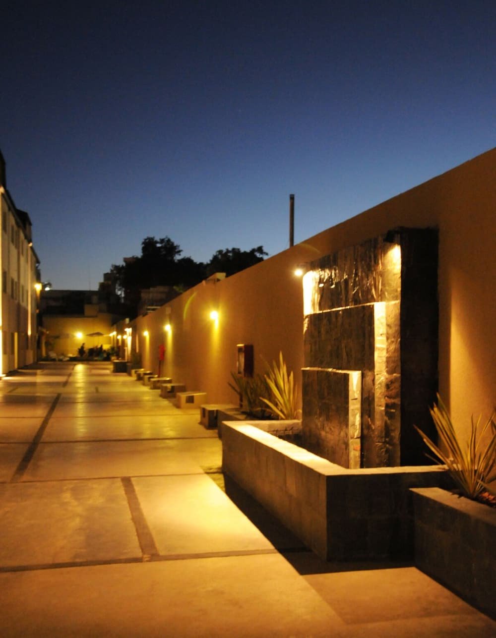 Pasillo nocturno con bancos, una fuente de agua y pared de piedra