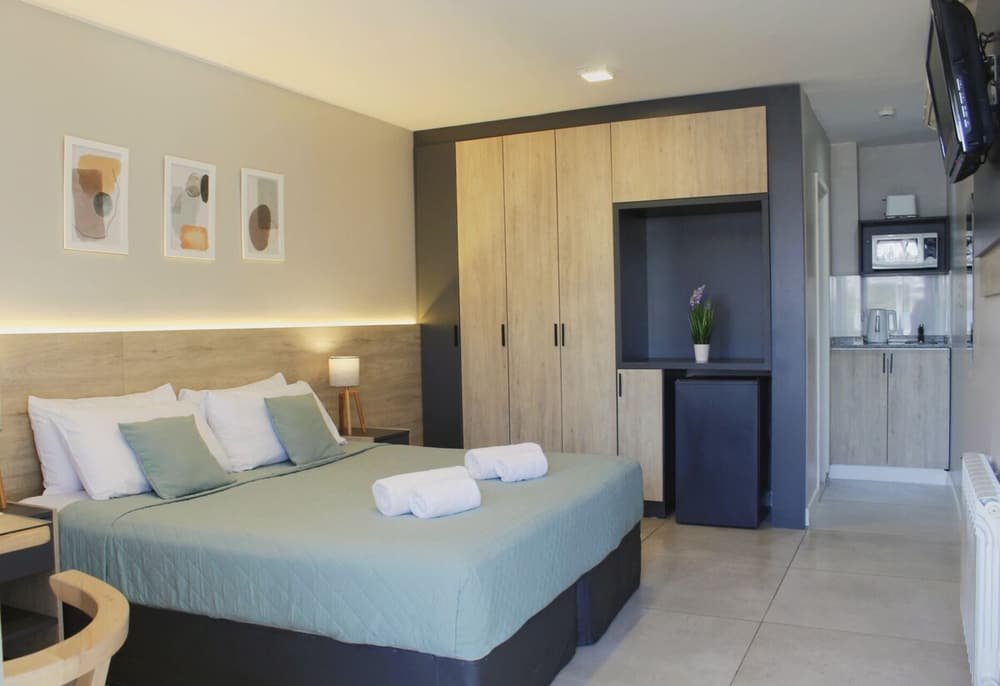 Habitación con cama, mesa de luz, lámpara, cuadro, placard y kitchenette