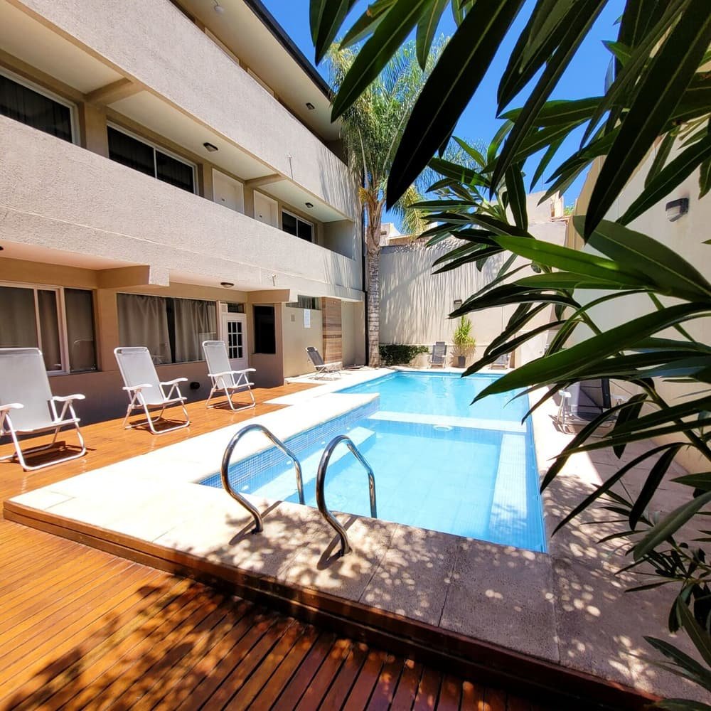Piscina con reposeras, deck de madera y edificio con balcones y ventanas