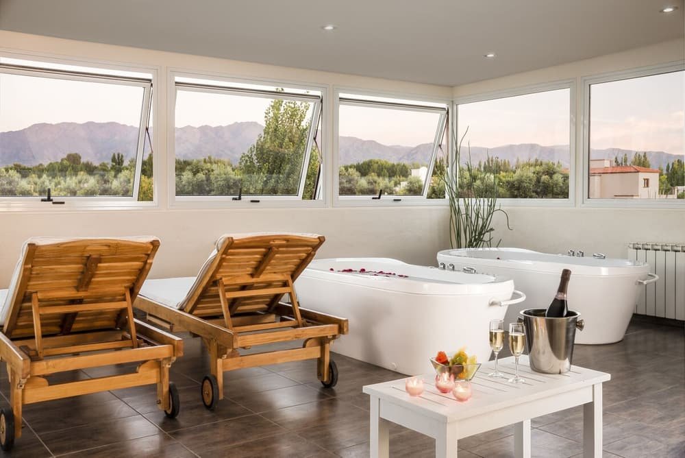 Sala de spa com duas espreguiçadeiras de madeira, banheira grande e garrafa de champanhe