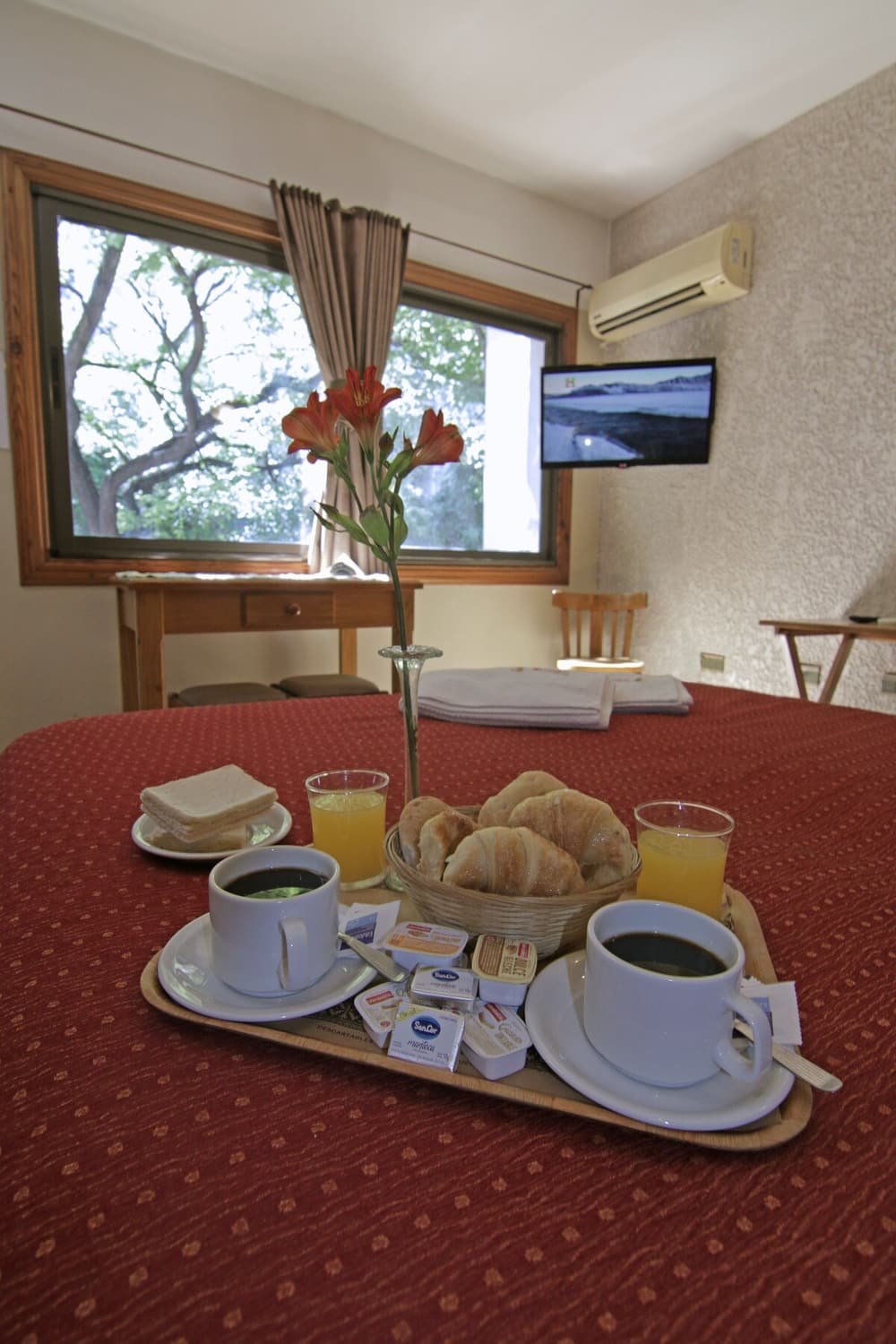 Bandeja de desayuno sobre una cama con medialunas, café, jugo y un florero
