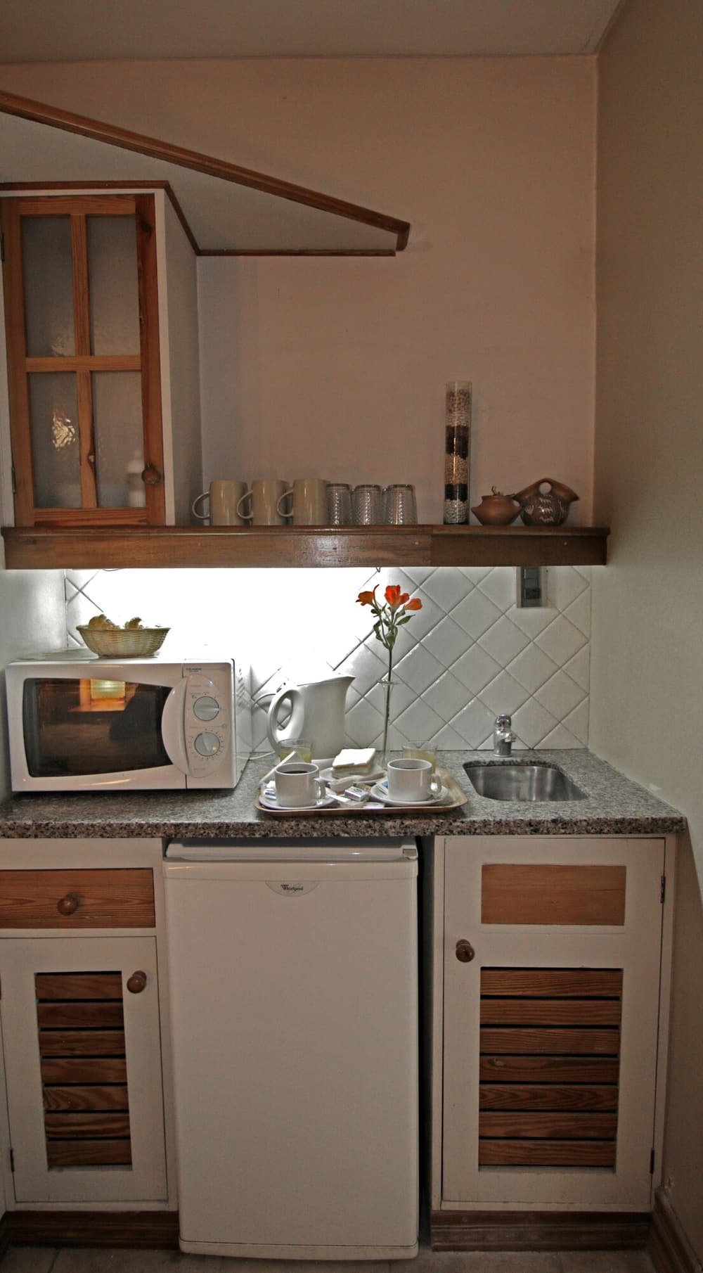 Cocina compacta con microondas, heladera pequeña, alacenas de madera y bacha